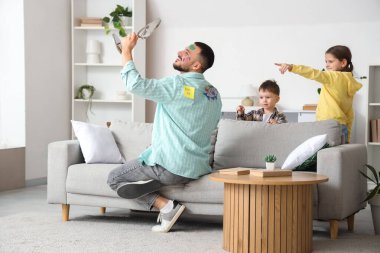 Küçük çocukları evde gülerken, yüzü resimlerle dolu mutlu bir baba aynaya bakıyor. 1 Nisan şakası.