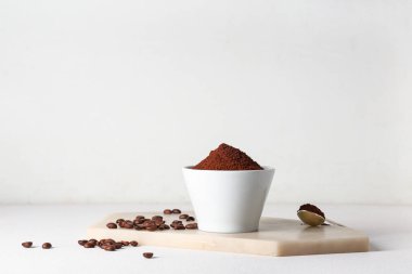 Bir kase kahve tozu, beyaz arka planda fasulye ve kaşık
