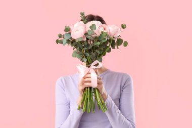 Elinde bir buket ranunculus çiçeği ve pembe arka planda okaliptüs olan genç bir kadın.