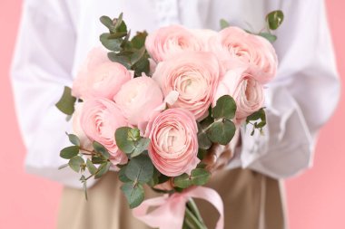 Pembe arka planda bir buket ranunculus çiçeği ve okaliptüs olan genç kadın, yakın plan.