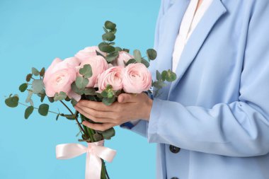 Mavi arka planda bir buket ranunculus çiçeği ve okaliptüs olan genç kadın, yakın plan.