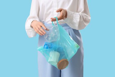 Mavi arka planda plastik eşyalar taşıyan kadın, yakın plan.