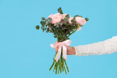 Mavi arka planda bir buket ranunculus çiçeği ve okaliptüs olan kadın eli.