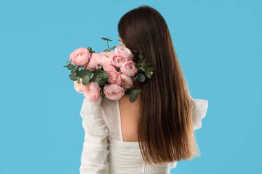 Mavi arka planda bir buket ranunculus çiçeği ve okaliptüs olan genç bir kadın.