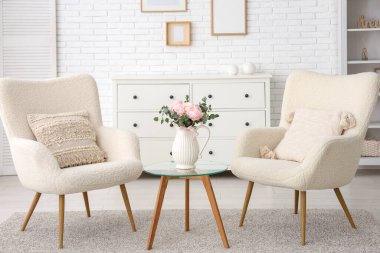 Beyaz koltukları ve kahve masasının üzerinde güzel ranunculus çiçekleri olan şık bir oturma odası.