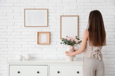 Genç bir kadın, oturma odasındaki çekmecelerin üzerine vazo ve güzel ranunculus çiçekleri koyuyor.