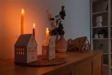 Karanlık odadaki çekmecelerde yanan mumlarla ev şekilli tutucular.