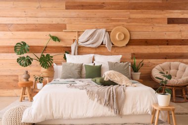 Büyük yatağı, bitkileri ve koltuğu olan rahat bir yatak odası.