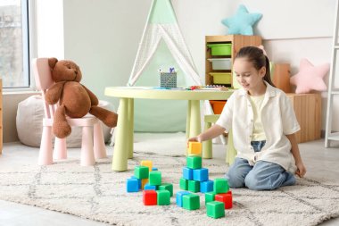 Evdeki halının üstünde küplerle oynayan tatlı bir kız.