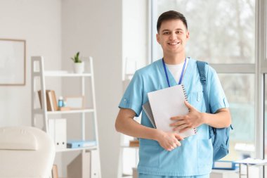 Klinikte not defterleri ve sırt çantalı bir erkek stajyer.