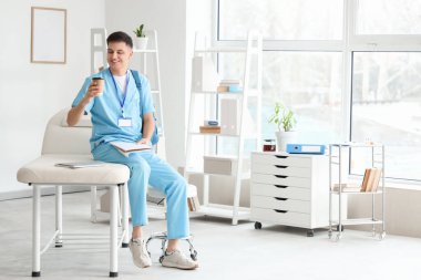 Klinikteki kanepede oturan defter ve kahve fincanı olan bir erkek stajyer.