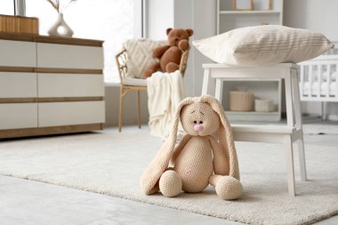 Oyuncak tavşan, çocuk odasında yastıklı tabureye yakın.