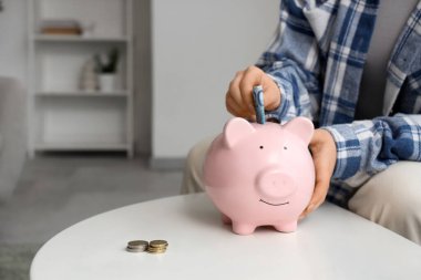 Genç bir kadın evdeki masadaki kumbaraya avroluk banknot yatırıyor.