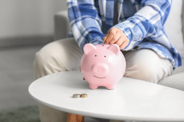 Genç bir kadın evdeki kumbaraya para koyuyor, yakın plan.