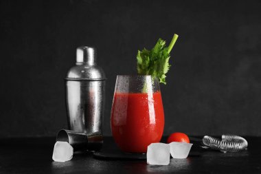 Bir bardak Bloody Mary, kereviz, buz küpleri, titretici, ölçü kabı ve domatesli siyah grunge arkaplan