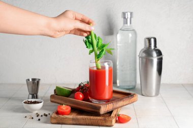 Kanlı Mary, kereviz, domates, karabiber ve beyaz fayans üzerinde ölçü kabıyla kadın eli.