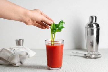 Beyaz arka planda, bir bardak Bloody Mary 'nin içine kereviz koyan kadın.