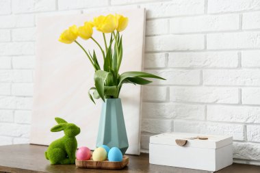 Vazoda lale çiçekleri, paskalya tavşanı ve beyaz tuğla duvarın yanında renkli yumurta tutacağı.