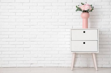 Beyaz tuğla duvarın yanındaki masada vazo dolusu güzel ranunculus çiçekleri.