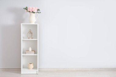 Beyaz duvarın yanındaki raflarda bir buket güzel ranunculus çiçeği olan vazo.