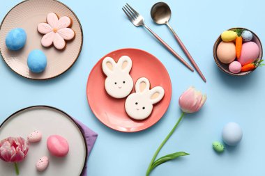 Tatlı kurabiyeler, paskalya yumurtaları ve mavi arka planda lale çiçekleri olan güzel bir masa.