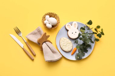 Tatlı kurabiyeler, Paskalya yumurtaları ve sarı arka planda okaliptüs dallarıyla güzel bir masa.