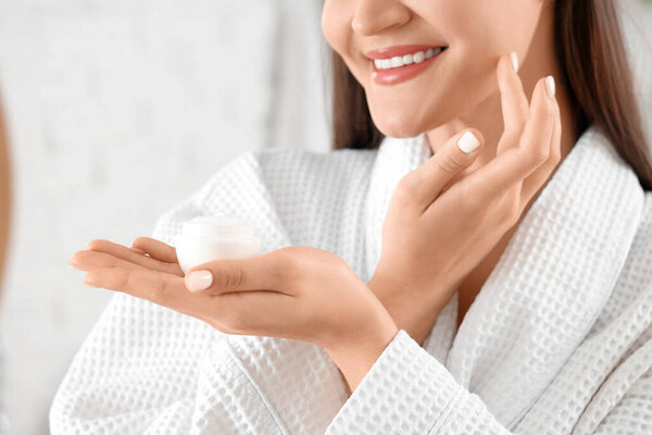 Молодая женщина наносит крем в ванной комнате, крупным планом