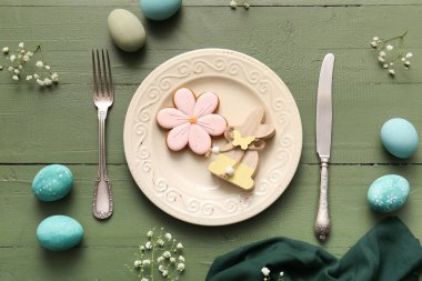 Tatlı kurabiyeli güzel bir masa, Paskalya yumurtaları ve yeşil ahşap arka planda çingene çiçekleri.