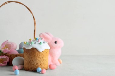 Hasır sepet, çiçekler, dekoratif tavşan, paskalya yumurtaları ve gri arka planda pasta.