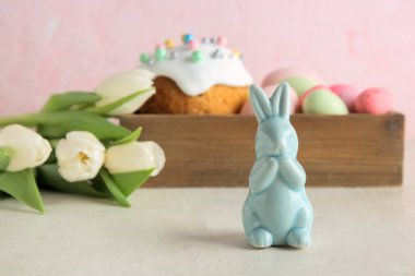 Dekoratif tavşancık, Paskalya yumurtası ve pasta gri masada, pembe duvarın yanında.