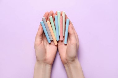 Mor arka planda bir sürü renkli tebeşir tutan kadın