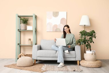 Genç bir kadın oturma odasındaki koltukta modern laptop kullanıyor.