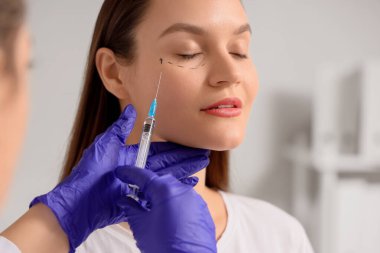 Yüzünde işaretler olan genç bir kadın klinikte iğne oluyor, yakın plan. Blepharoplasty konsepti