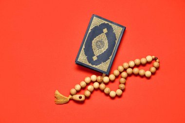 Kırmızı arka planda tespih taşıyan bir Kur 'an. Ramazan kutlaması