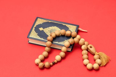 Kırmızı arka planda tespih boncukları olan Kur 'an, yakın plan. Ramazan kutlaması