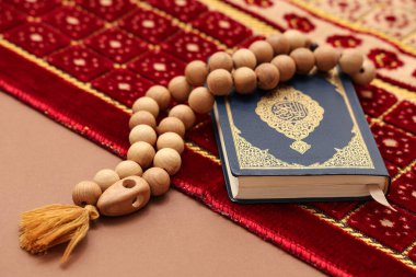 Kur 'an' da tespih ve kahverengi arka planda halı, yakın plan. Ramazan kutlaması