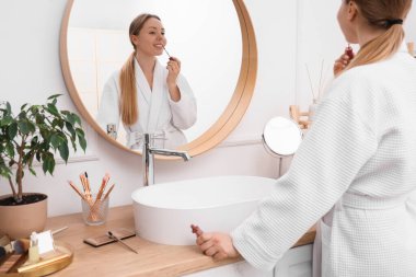 Banyoda aynanın yanında ruj süren genç bir kadın.