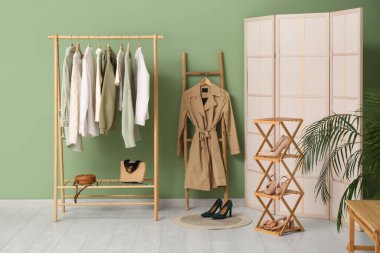 Merdivende şık kıyafetler ve odada yeşil duvarın yanında katlanmış bir ekran var.