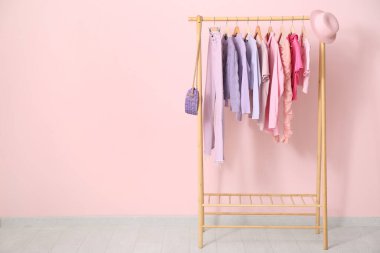 Odada pembe duvarın yanında şık kıyafetler var.