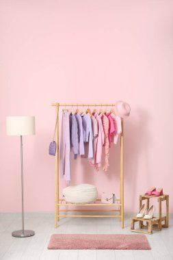 Şık kıyafetler, lamba ve pembe duvarın yanında duran ayakkabılar.