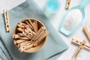 Beyaz zemin üzerinde deterjan, kumaş ve çamaşır tozu olan bir kase ahşap mandal.