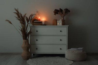 Karanlık odada yanan mumlar, vazolar ve çiçeklerle dolu çekmeceler.