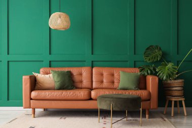 İçinde kahverengi kanepe, puf ve palmiye bitkisi olan bir oturma odası.