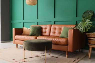 İçinde kahverengi kanepe, puf ve palmiye bitkisi olan bir oturma odası.