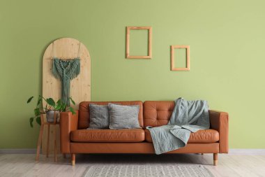 Kahverengi kanepe, oturma odasının iç tarafındaki yeşil duvarın yanında yastıklar ve ekoseli.