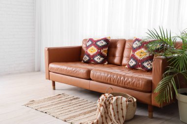 Oturma odasının içinde kahverengi kanepe, palmiye ağacı ve penceresi var.