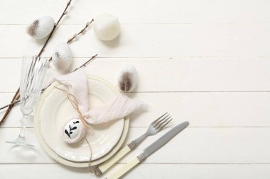 Beautiful table setting with Easter eggs, feathers and pussy willow branches on white wooden background