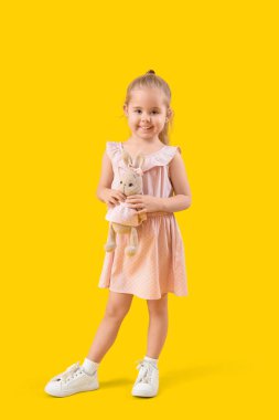 Sarı arka planda oyuncak tavşanı olan sevimli küçük bir kız.