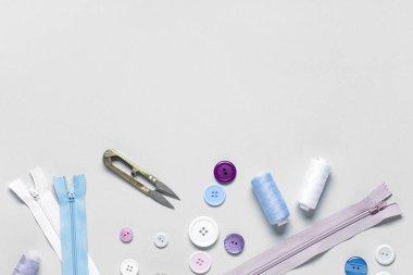 Gri arkaplanda iplik makaralı, fermuarlı ve makaslı farklı renkli düğmeler