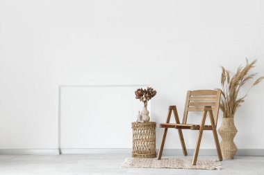 Sandalye, otlar ve çiçekler odadaki beyaz duvarın yanındaki vazoda kahve masasının üzerinde.